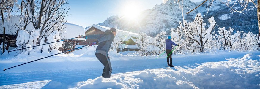 Zwei Personen beim Langlaufen in verschneiter Berglandschaft bei Sonnenschein