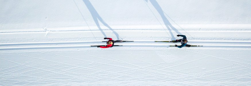 Zwei Langläufer auf schneebedeckter Loipe von oben mit langen Schatten
