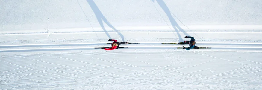 Zwei Langläufer auf schneebedeckter Loipe von oben mit langen Schatten