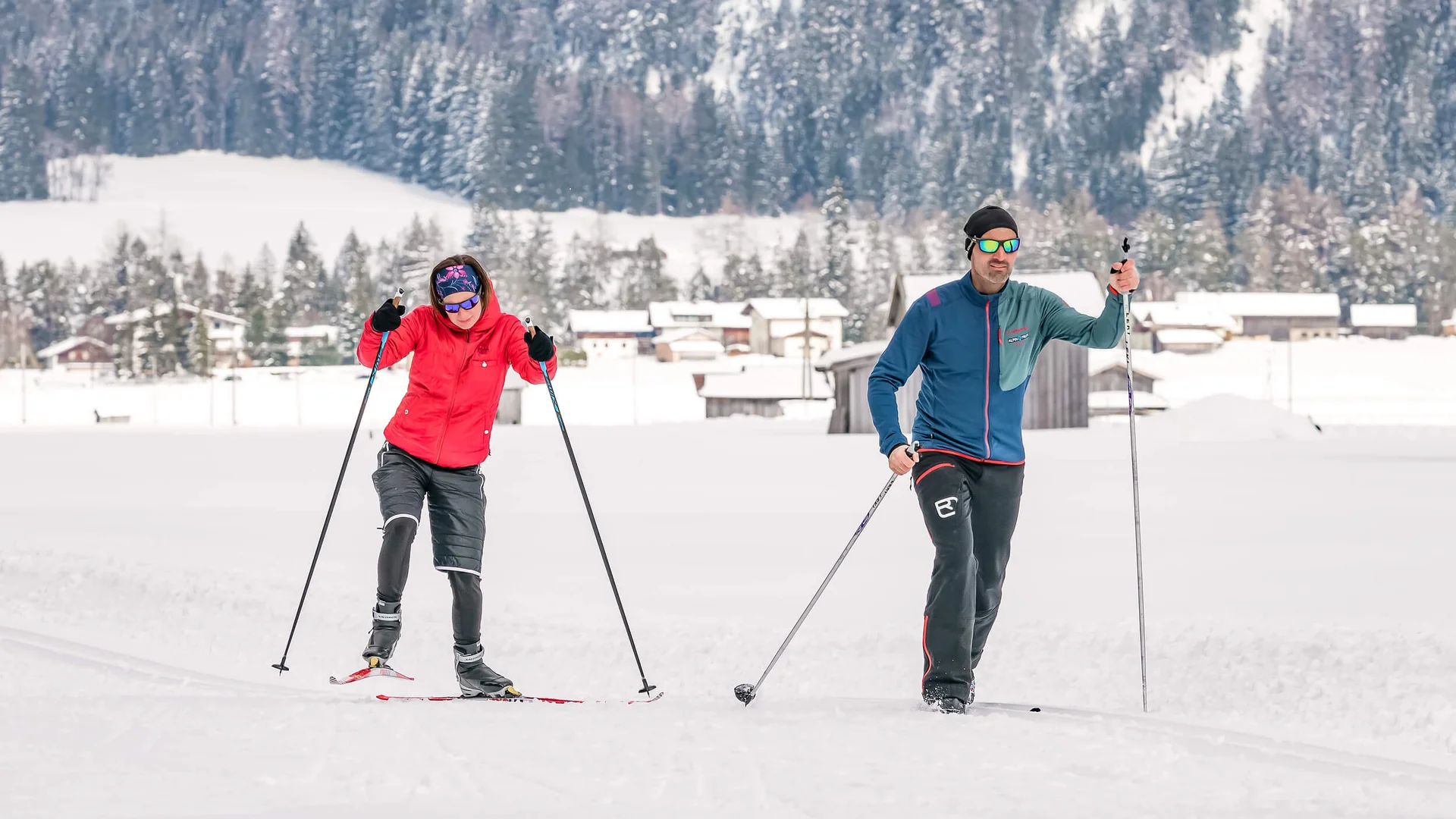 Loipen & Loipenbericht © Lechtal Tourismus / Radomir Gabric Zwei Personen beim Langlaufen auf verschneiter Landschaft mit Häusern und Wäldern im Hintergrund