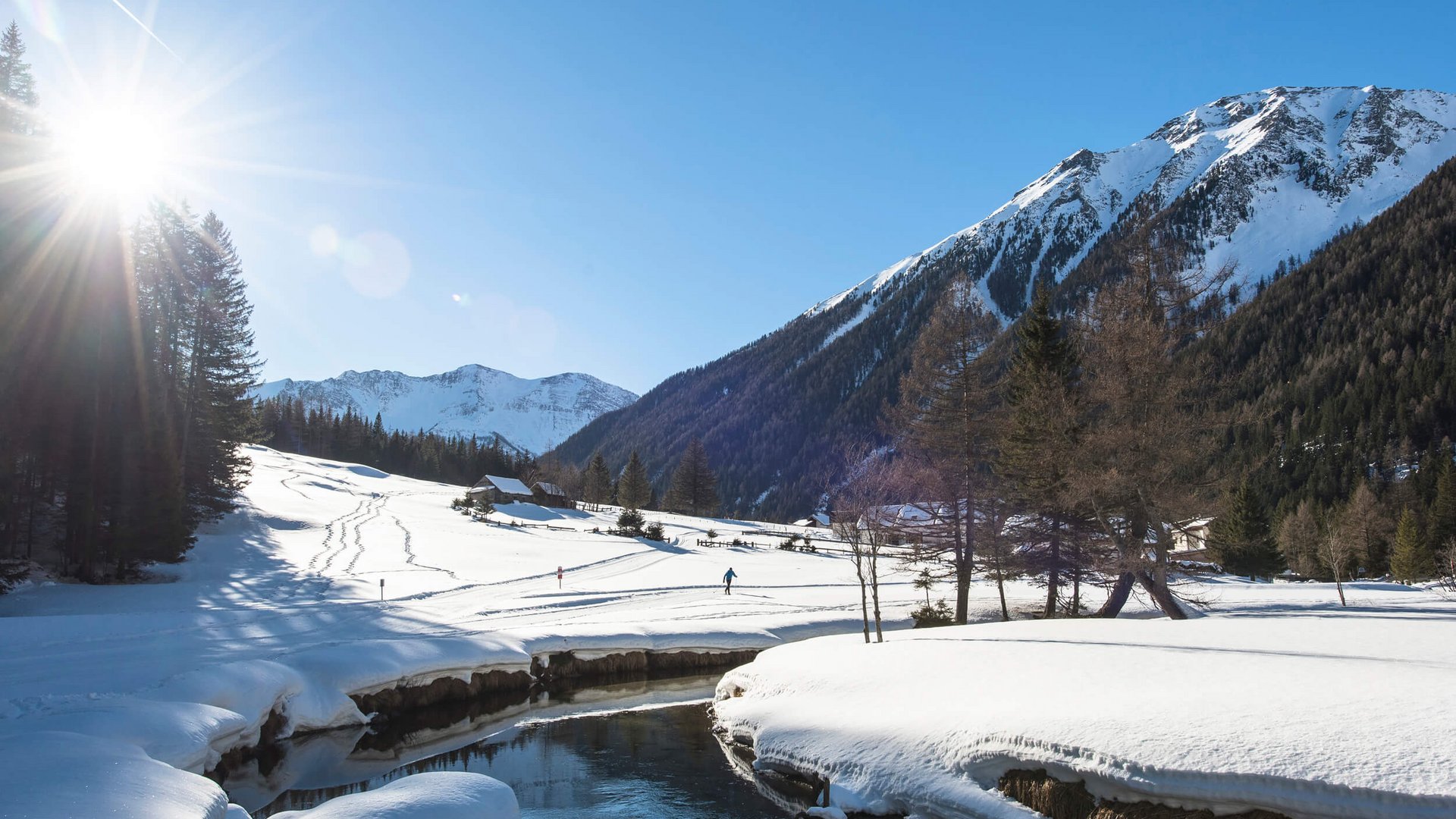Schneebedecktes Tal mit Bergen, Fluss und Person beim Skilanglauf