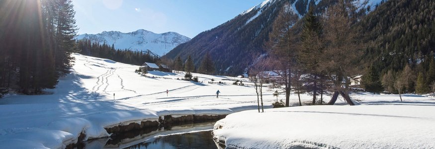 Schneebedecktes Tal mit Bergen, Fluss und Person beim Skilanglauf