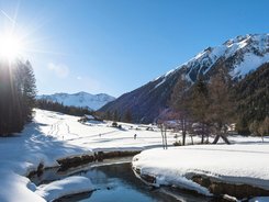 Snow-covered valley with mountains, river, and person cross-country skiing