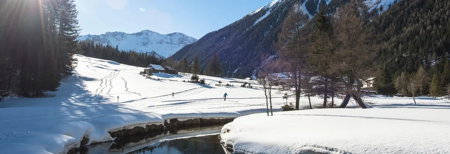 Schneebedecktes Tal mit Bergen, Fluss und Person beim Skilanglauf