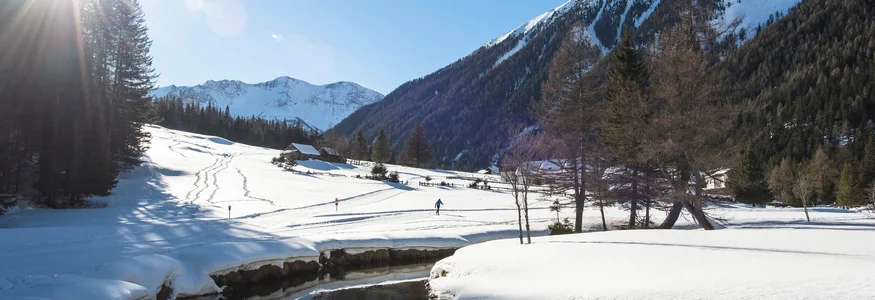 Schneebedecktes Tal mit Bergen, Fluss und Person beim Skilanglauf