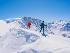 Two ski tourers hiking on snow-covered mountain on a sunny winter day
