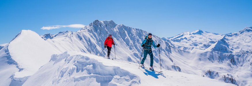Two ski tourers hiking on snow-covered mountain on a sunny winter day