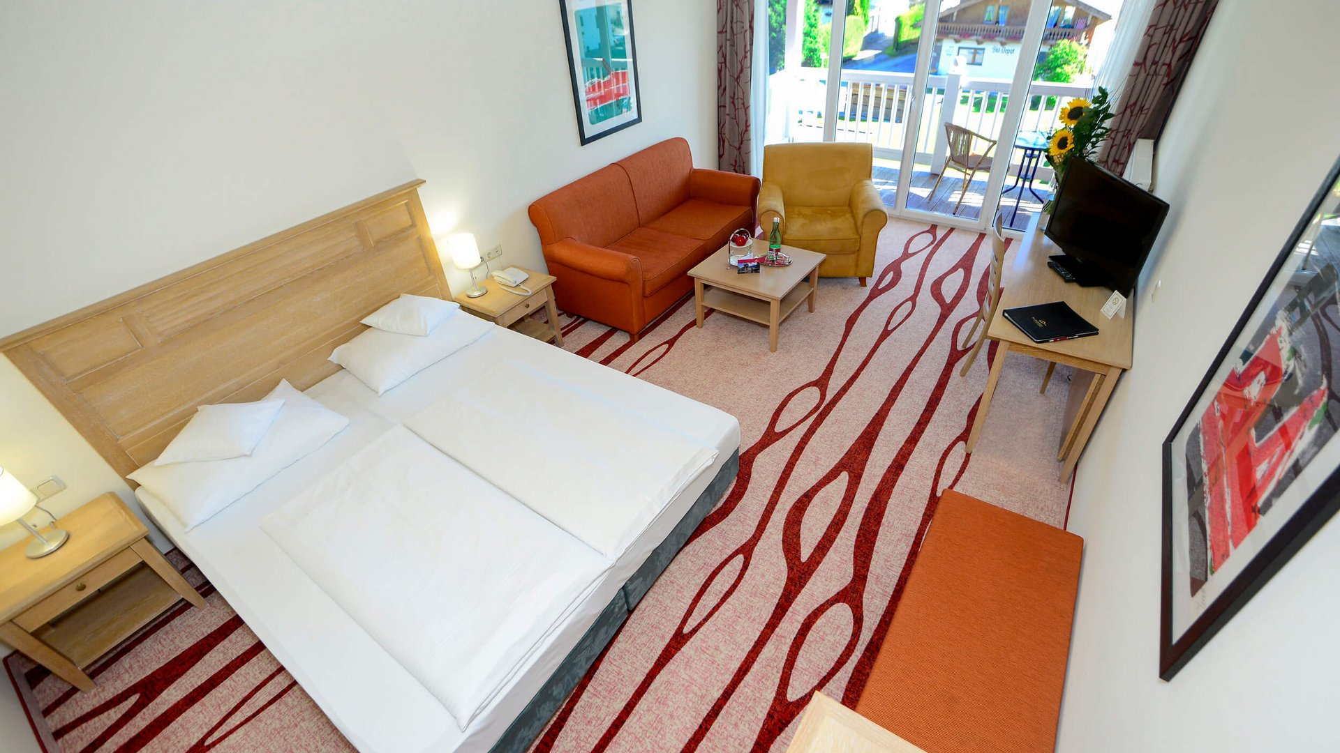 Modern hotel room with double bed, sofa, armchairs, and balcony