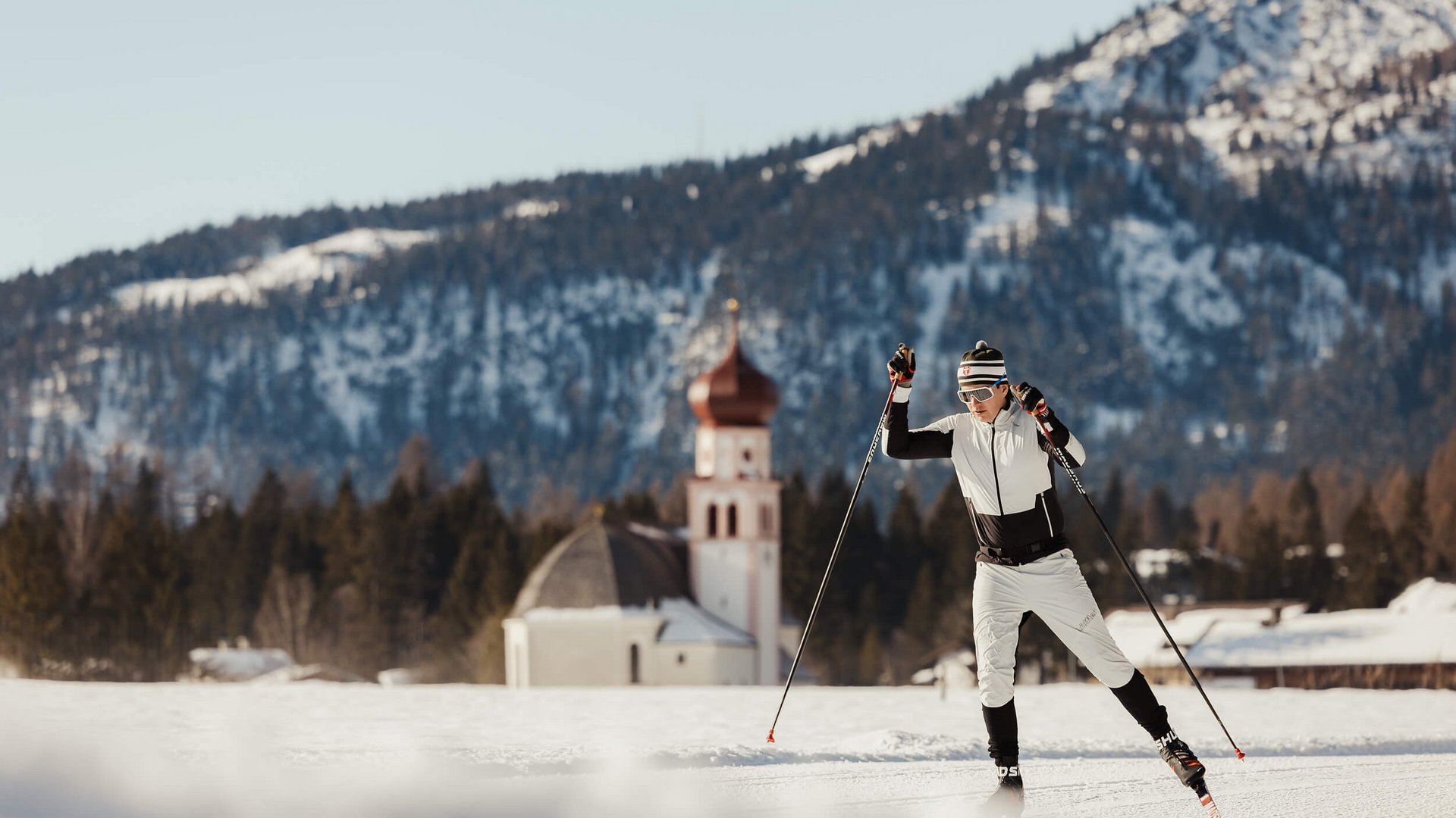 Skilangläufer vor verschneiter Berglandschaft mit Kirche im Hintergrund