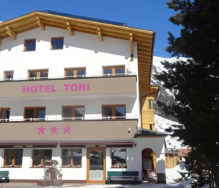 Außenansicht von Hotel Toni mit Bergen und Schnee im Hintergrund