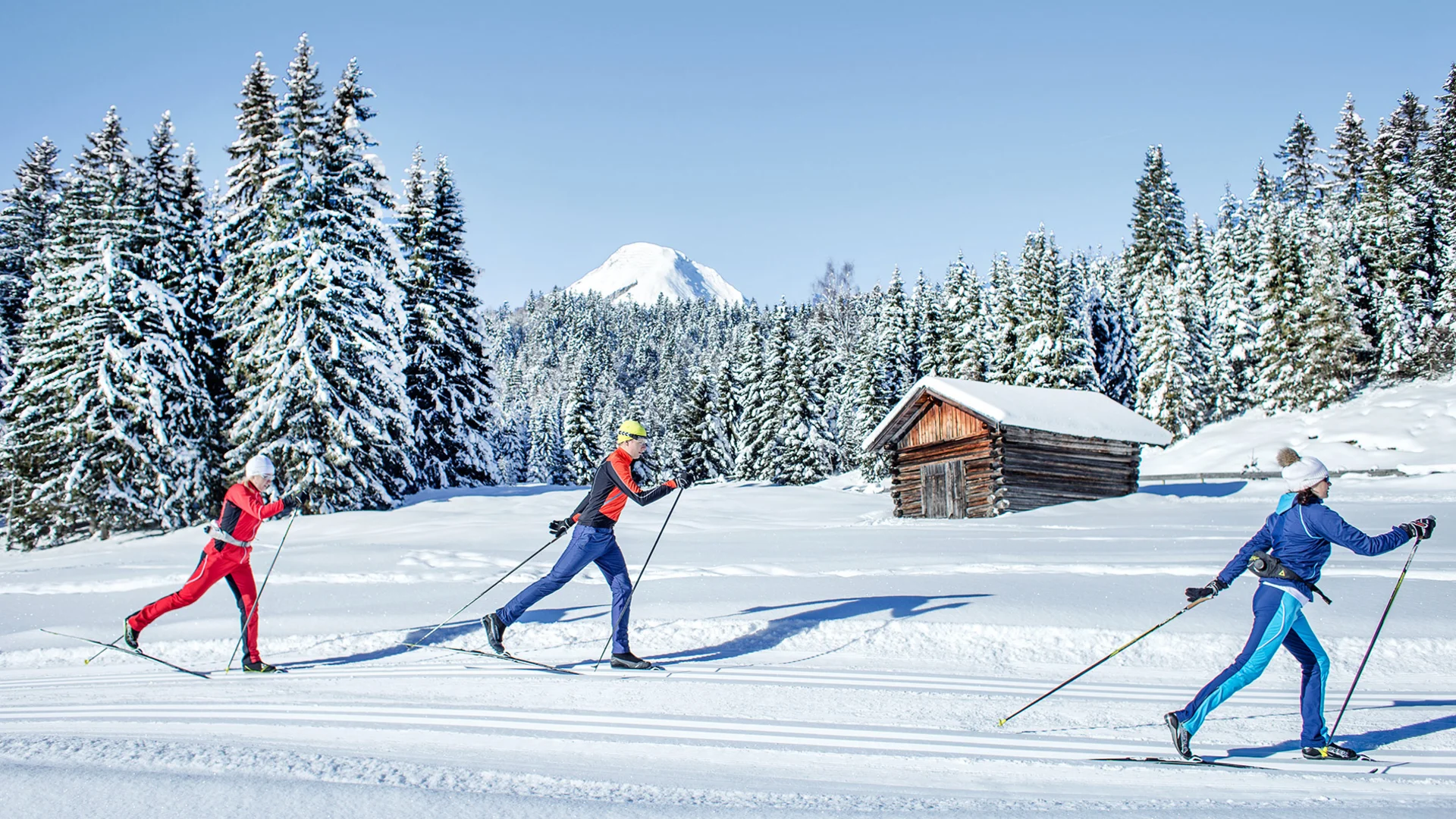 Winter-Schnuppertage im Alpenhotel Karwendel © Region Seefeld - Hannes Dabernig Drei Langläufer auf einer verschneiten Loipe vor Wald, Berghütte und schneebedecktem Gipfel