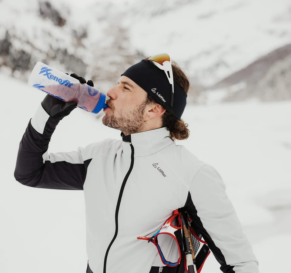 Sporternährung für längere Ausdauer © Alex Moling Mann in Winterkleidung trinkt aus einer Trinkflasche im verschneiten Gebirge