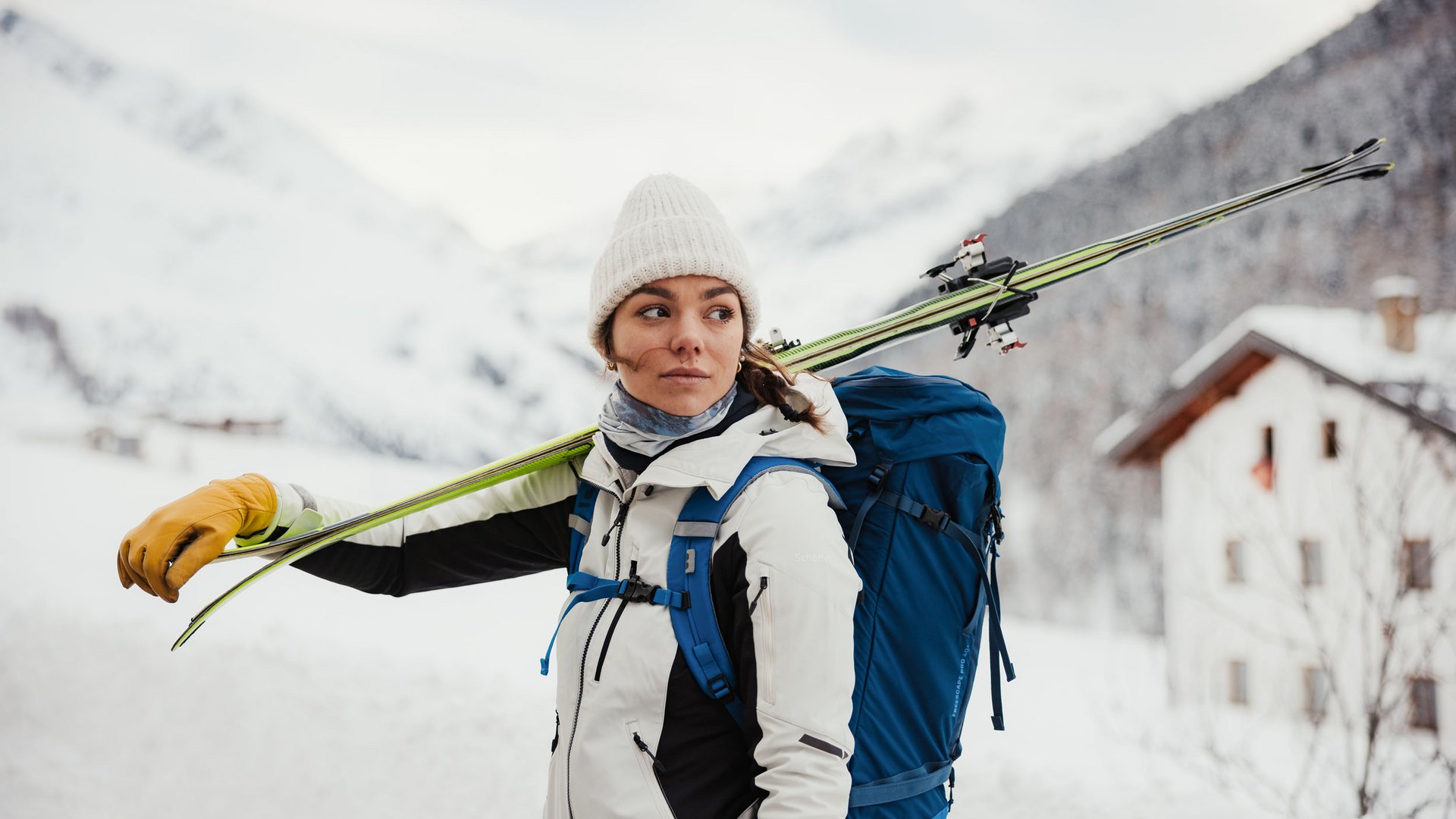 Frau mit Ski auf Schulter und Rucksack in verschneiter Berglandschaft