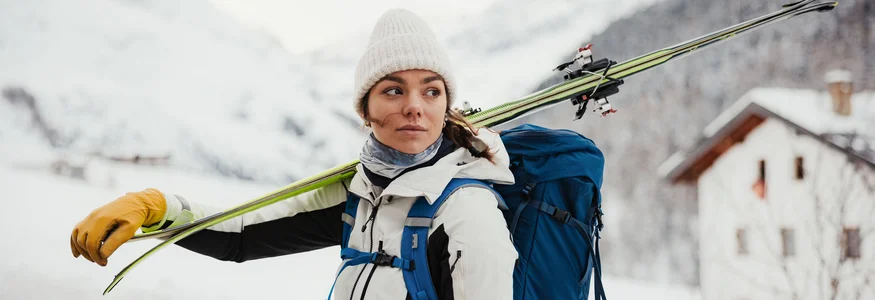 Frau mit Ski auf Schulter und Rucksack in verschneiter Berglandschaft