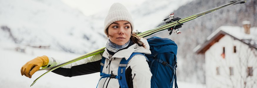 Frau mit Ski auf Schulter und Rucksack in verschneiter Berglandschaft