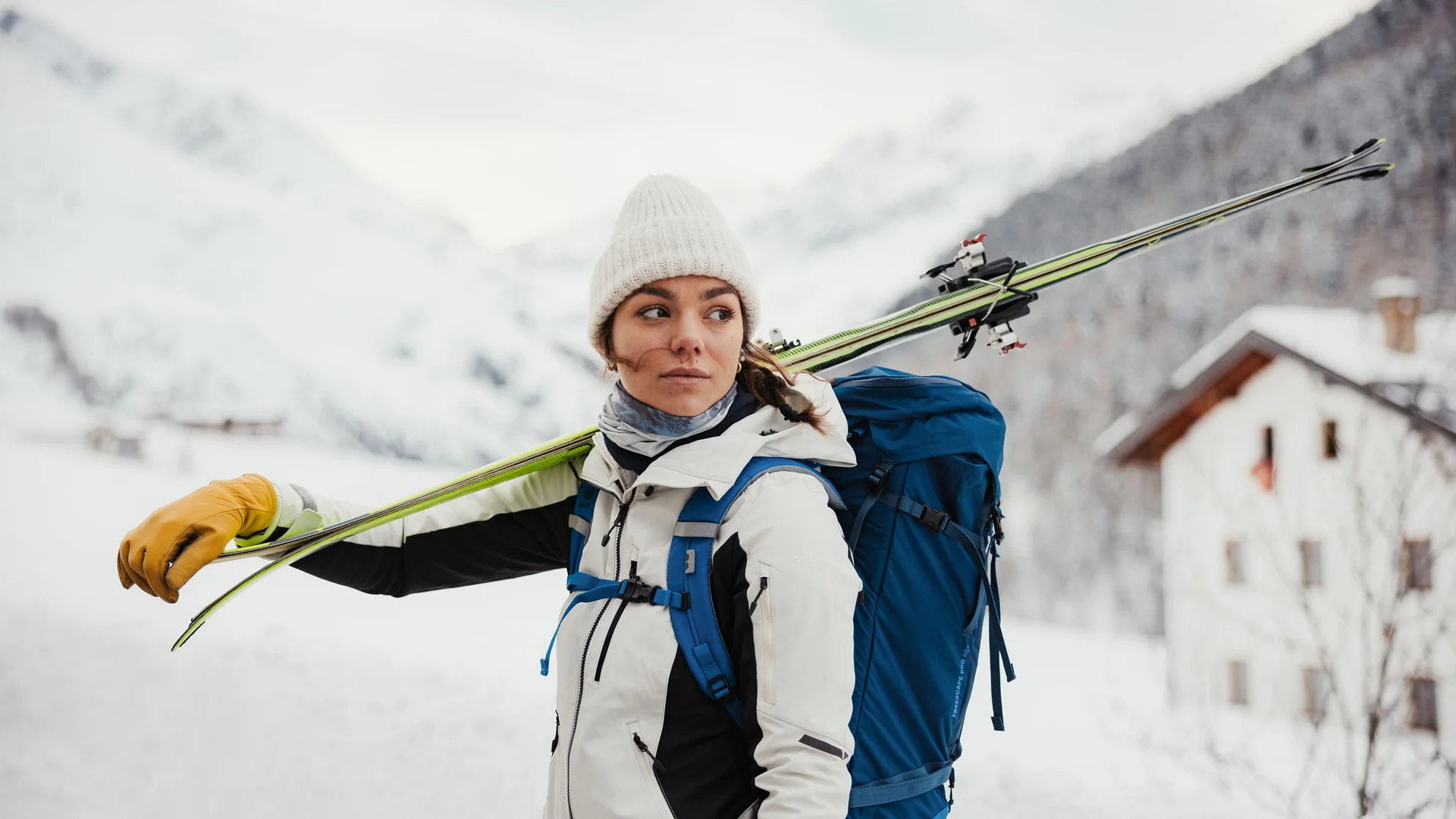 Frau mit Ski auf Schulter und Rucksack in verschneiter Berglandschaft
