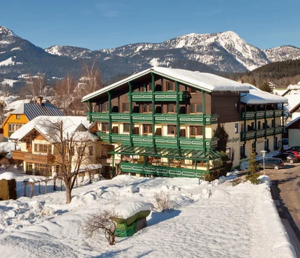 Hotel Kogler © Marcel Musiol Verschneites Dorf mit traditionellem grünem Gebäude vor Bergkulisse