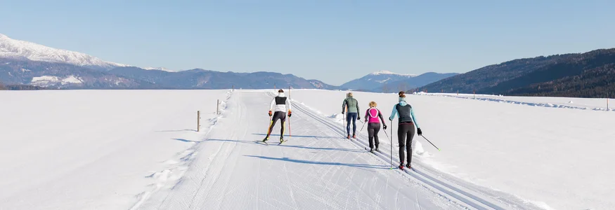 Salzburger Lungau © Salzburger Lungau Vier Personen beim Langlaufen auf schneebedeckter Loipe bei klarem Himmel