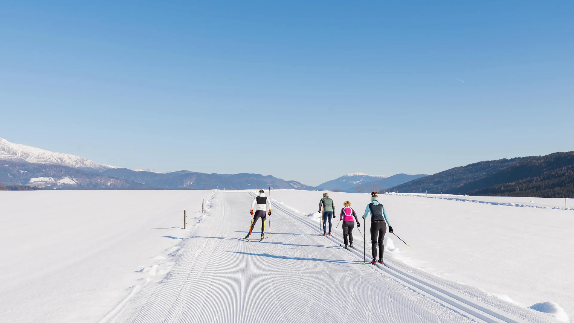 Langlauf Urlaub im Salzburger Lungau © Salzburger Lungau Vier Personen beim Langlaufen auf schneebedeckter Loipe bei klarem Himmel