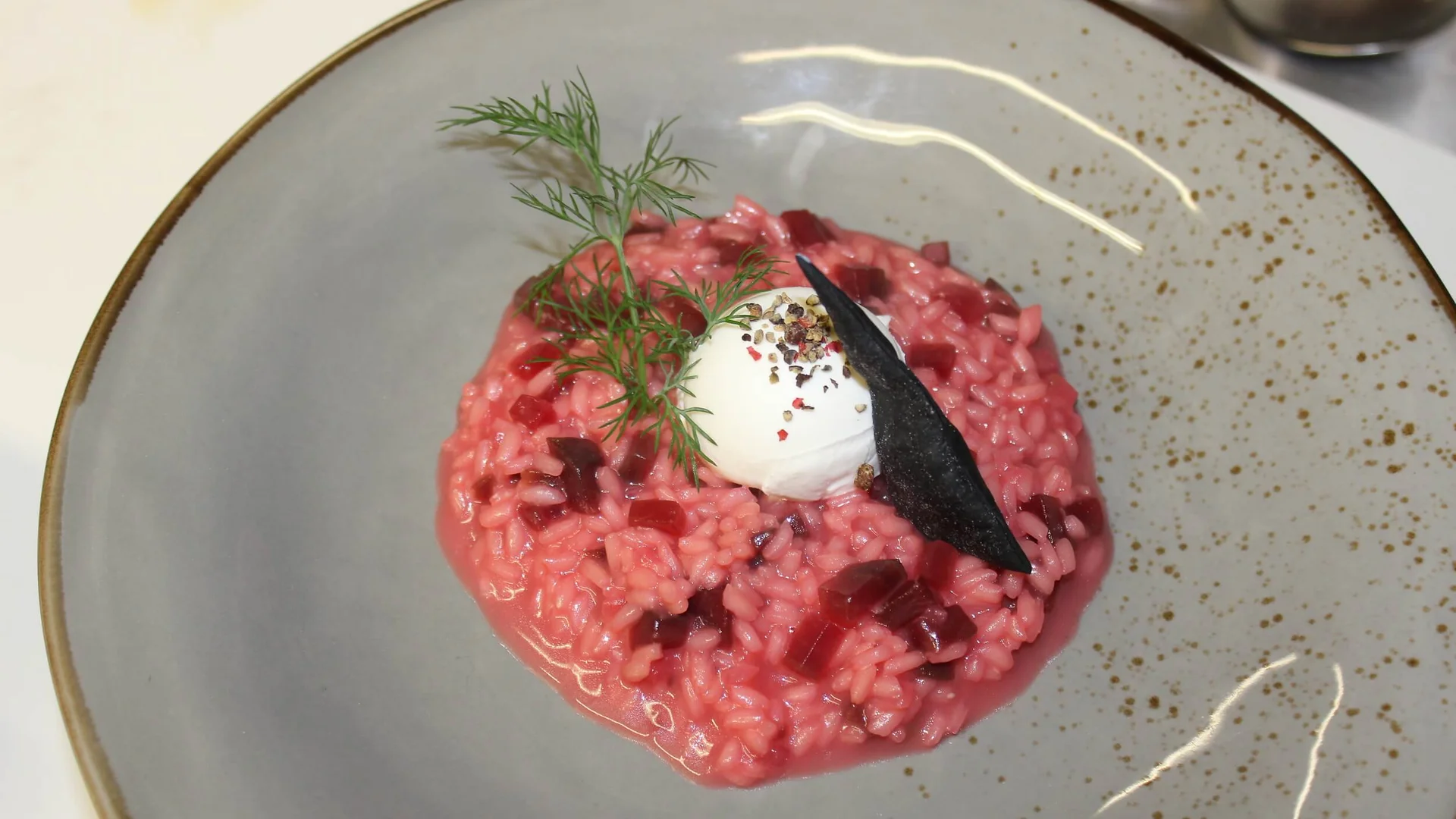 Rote Risotto mit Kräuterzweig und Frischkäse auf einem Teller angerichtet