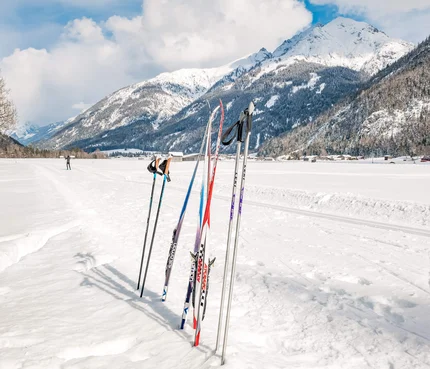 Cross-country skis and poles standing in snow with snowy mountains