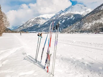 Cross-country skis and poles standing in snow with snowy mountains