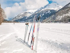 Cross-country skis and poles standing in snow with snowy mountains