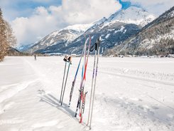 Cross-country skis and poles standing in snow with snowy mountains