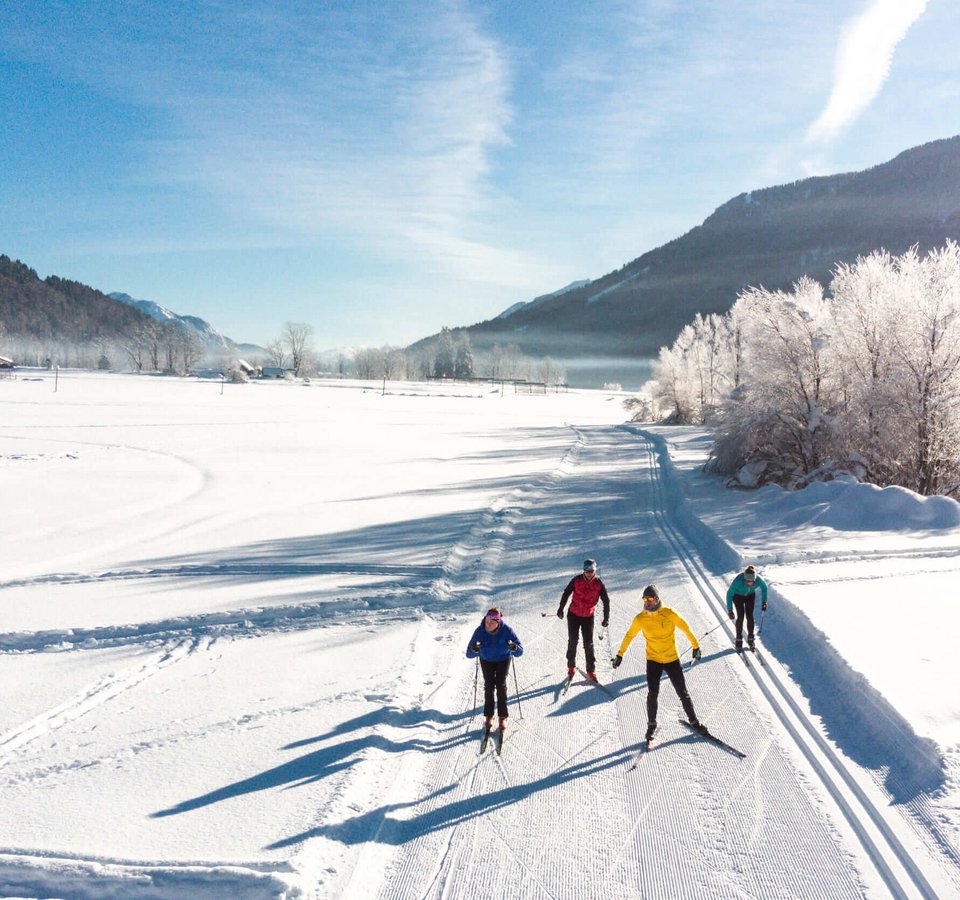 Vier Skifahrer auf einer Loipe in winterlicher Berglandschaft bei Sonnenschein