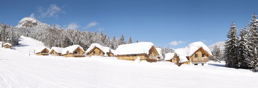 Snow-covered wooden cabins and trees under a clear blue sky