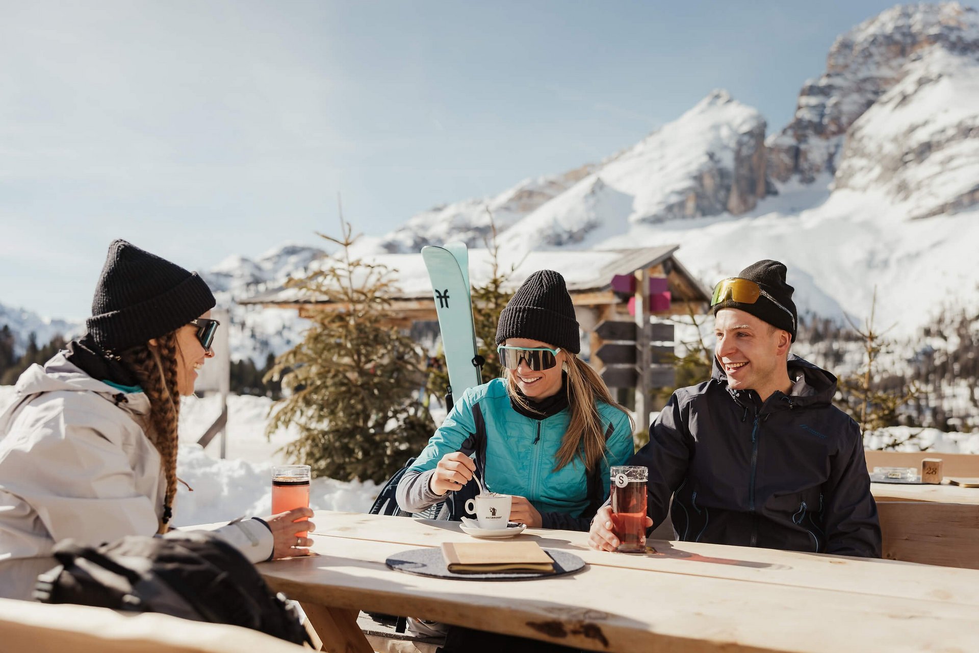 Drei Personen genießen Getränke draußen mit verschneiten Bergen im Hintergrund