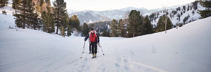Zwei Wanderer mit Stöcken wandern durch verschneite Berglandschaft