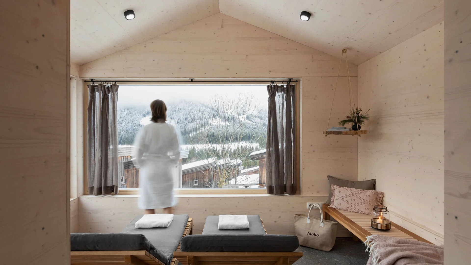 SLOHO Bergurlaub Apartments © Cathrine Stukhard Person im weißen Bademantel vor Fenster mit verschneiter Landschaft