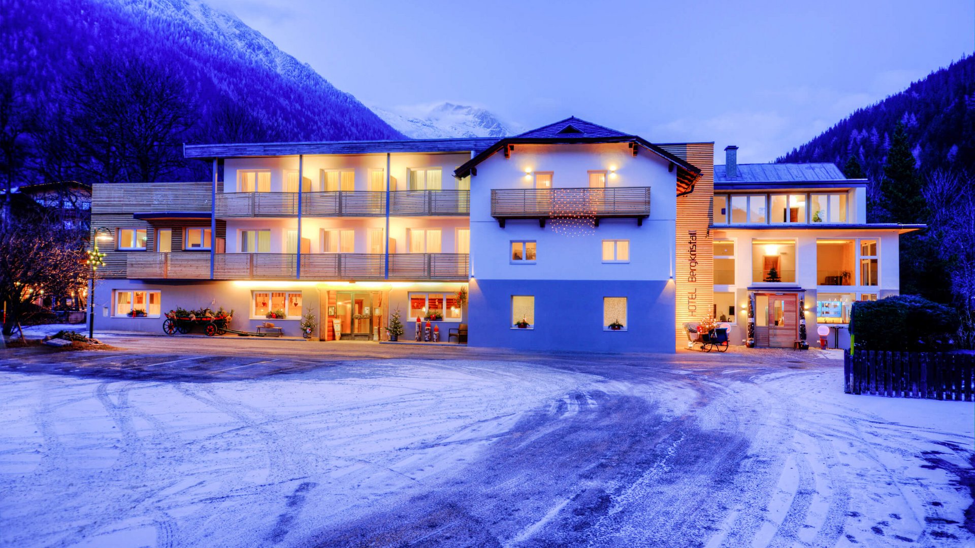 Lit hotel building with snow and mountains in the background at dusk