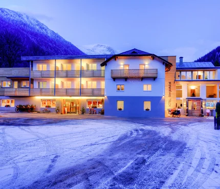 Beleuchtetes Hotel vor schneebedeckten Bergen am Abend