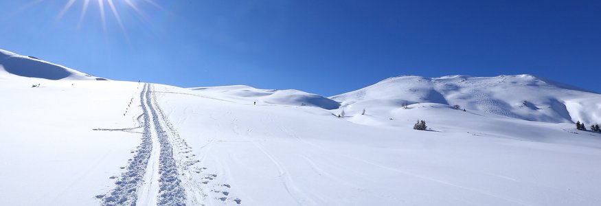 Sonnenstrahl über verschneiter Berglandschaft mit Skispuren im Schnee
