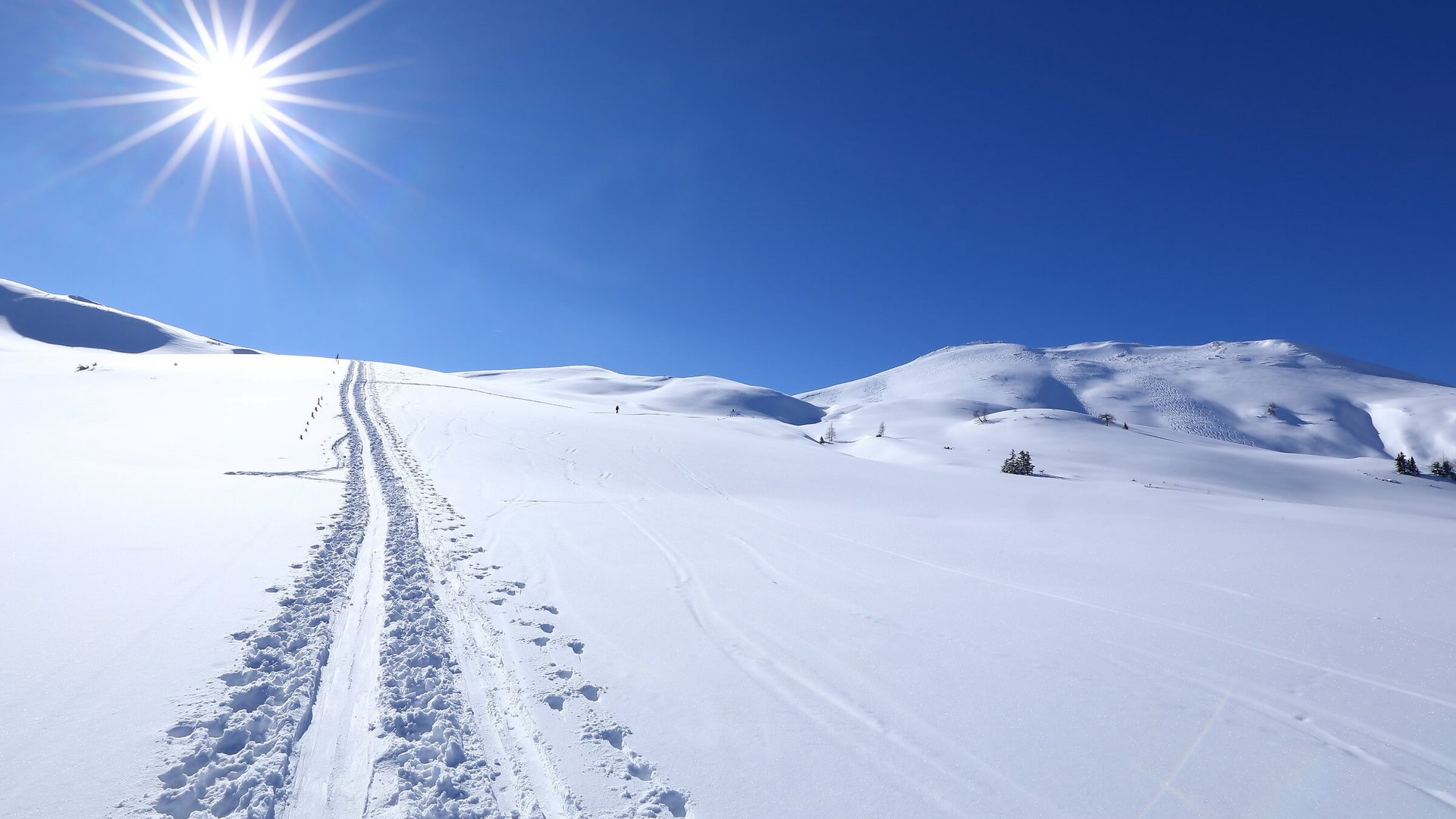 Sonnenstrahl über verschneiter Berglandschaft mit Skispuren im Schnee