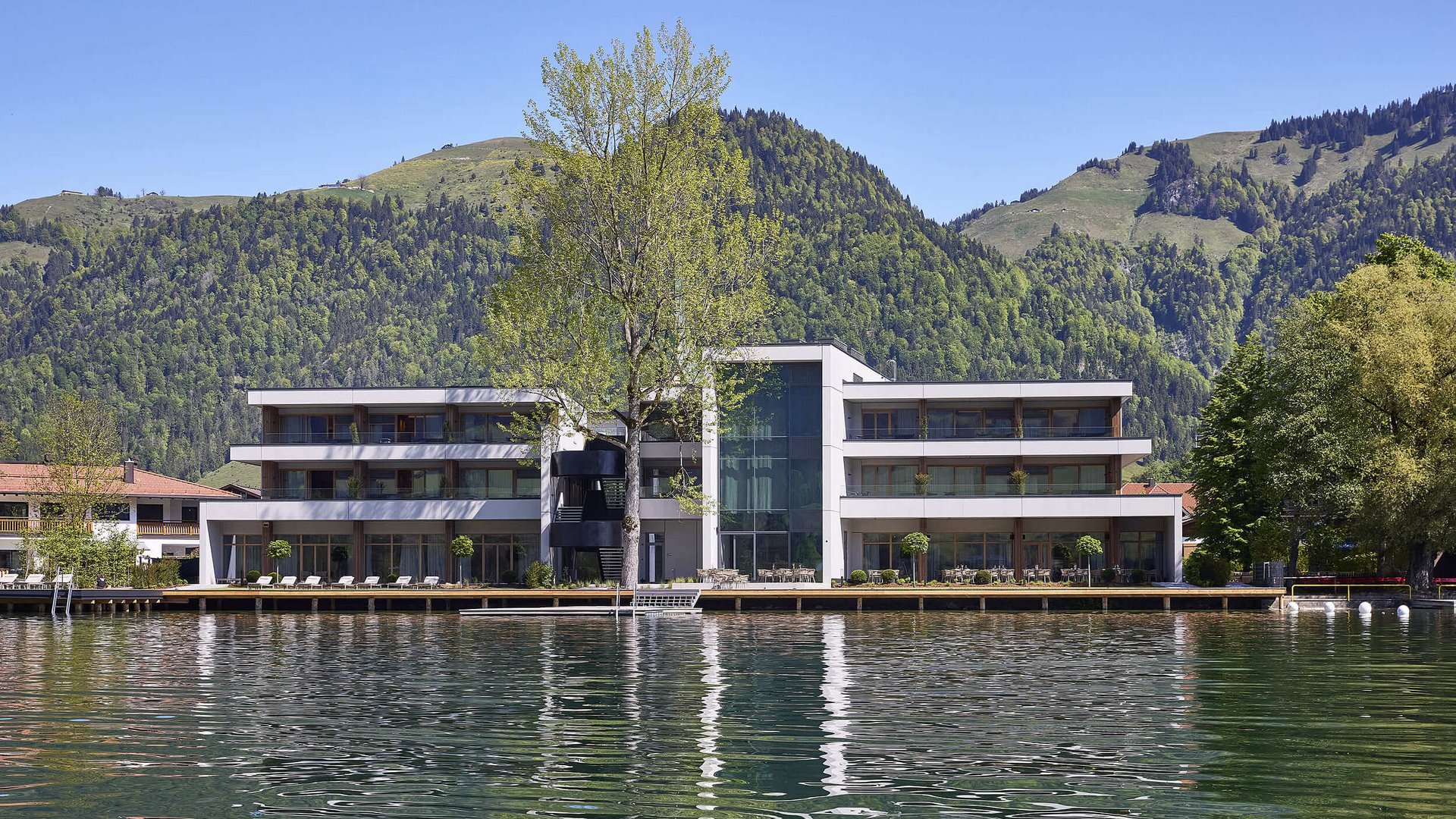Modern hotel on lake shore with mountain backdrop and clear sky