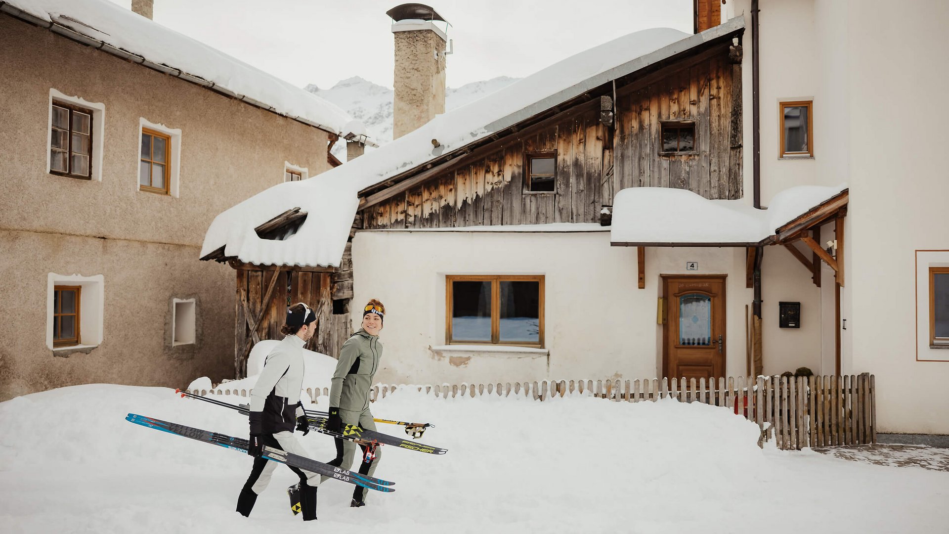 Zwei Langläufer tragen Ski durch verschneites Dorf