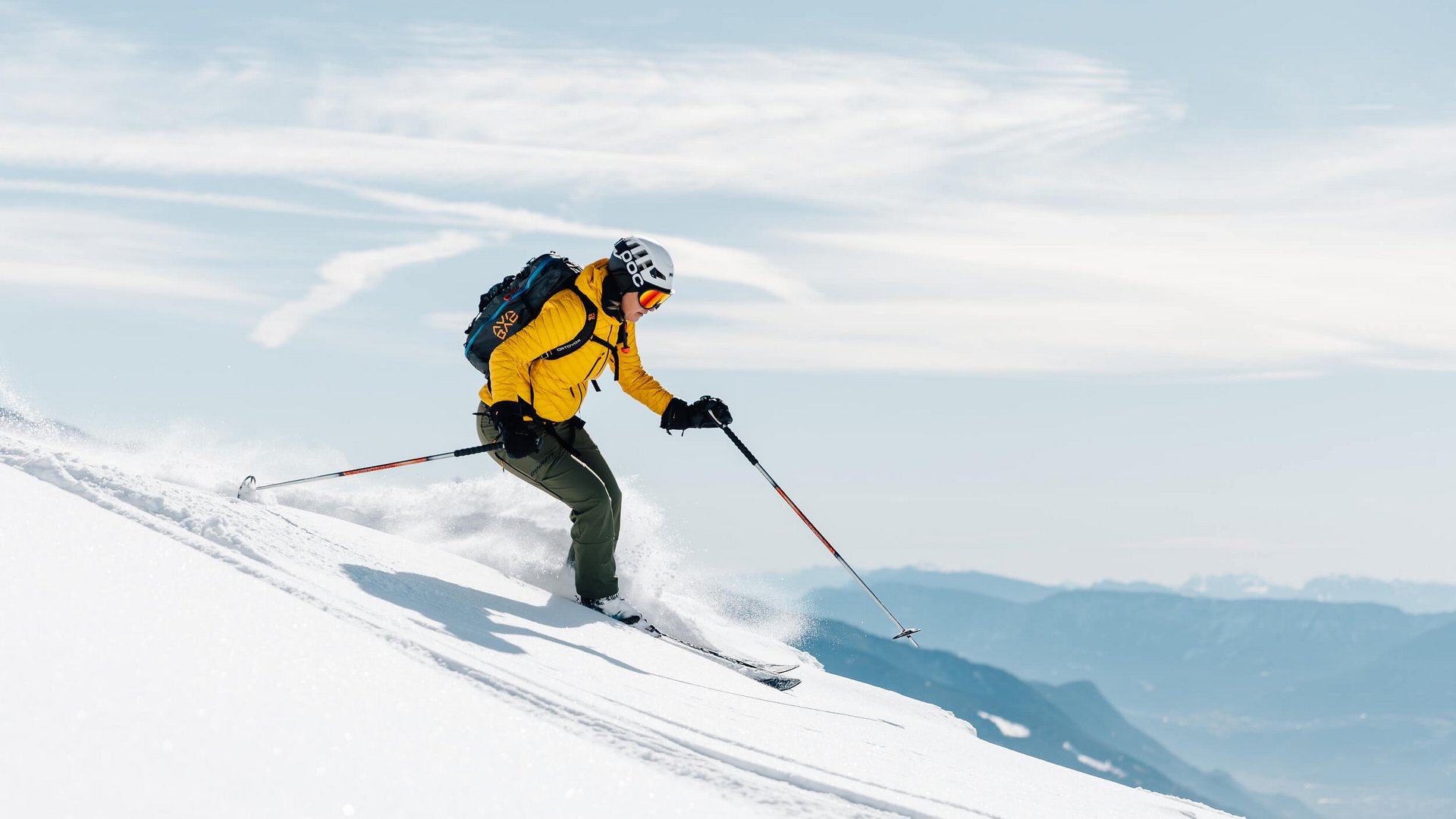 Skifahrer in gelber Jacke fährt einen schneebedeckten Hang hinab