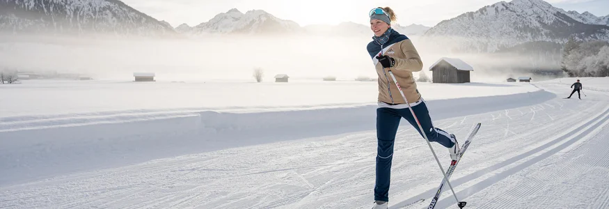 Frau beim Skilanglauf vor verschneiter Berglandschaft