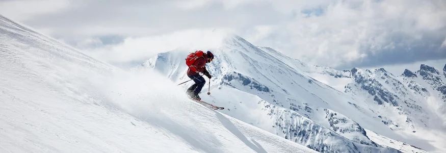 Skier descending snowy slope with mountains in the background