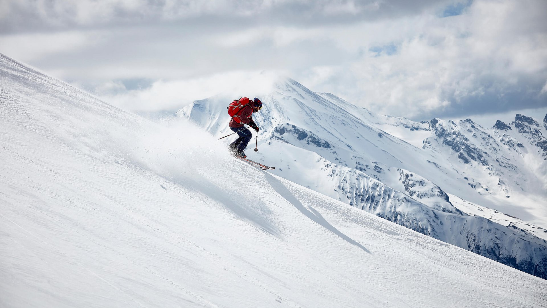 Skier descending snowy slope with mountains in the background