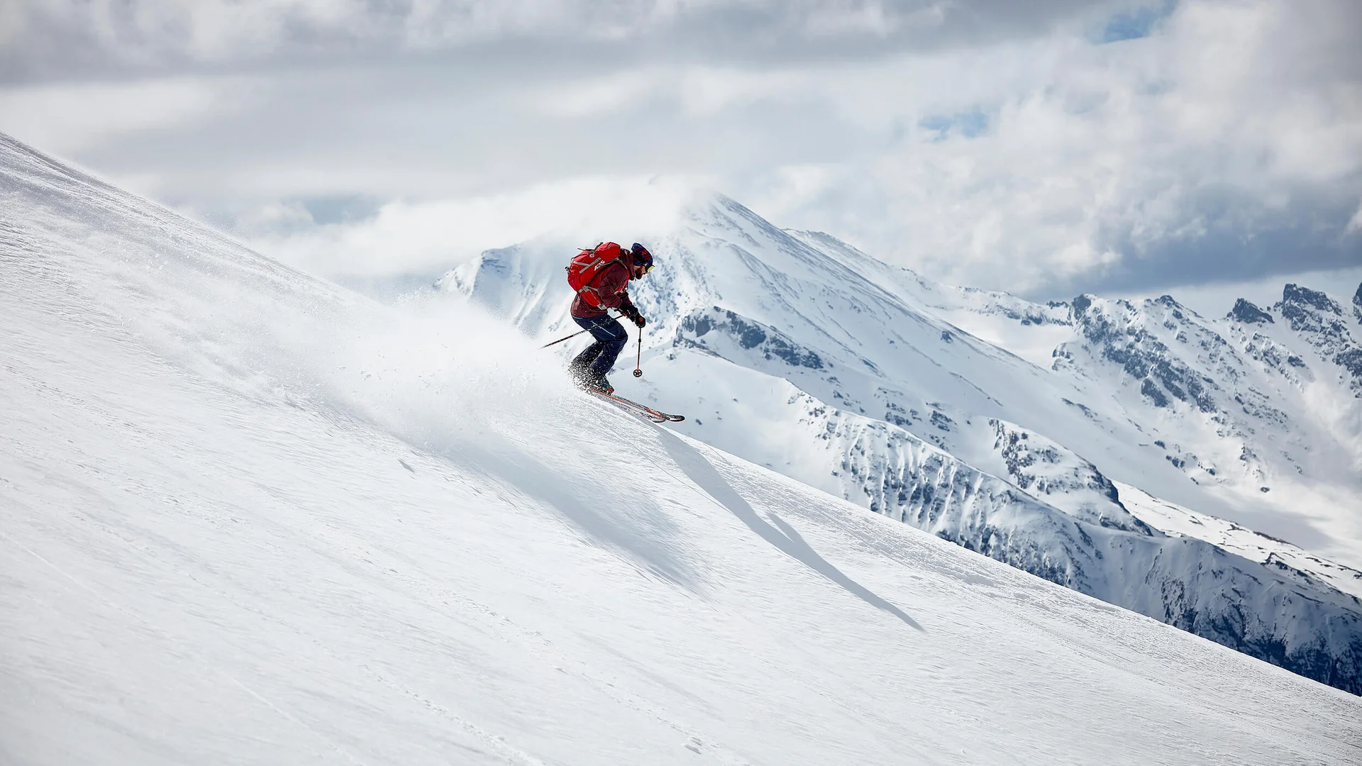 Skifahrer fährt den verschneiten Berghang mit Bergen im Hintergrund hinunter