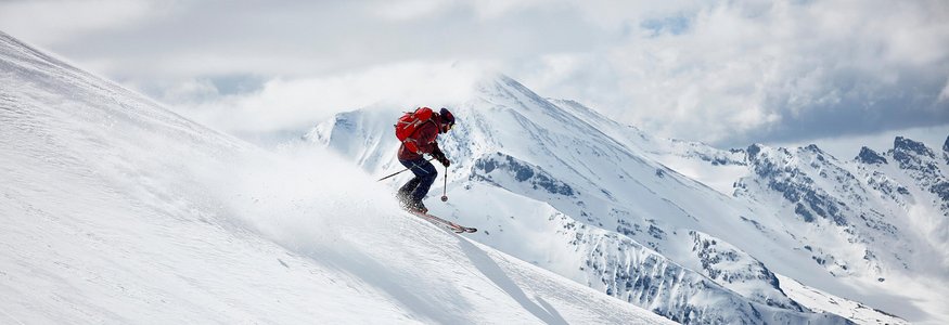 Skier descending snowy slope with mountains in the background