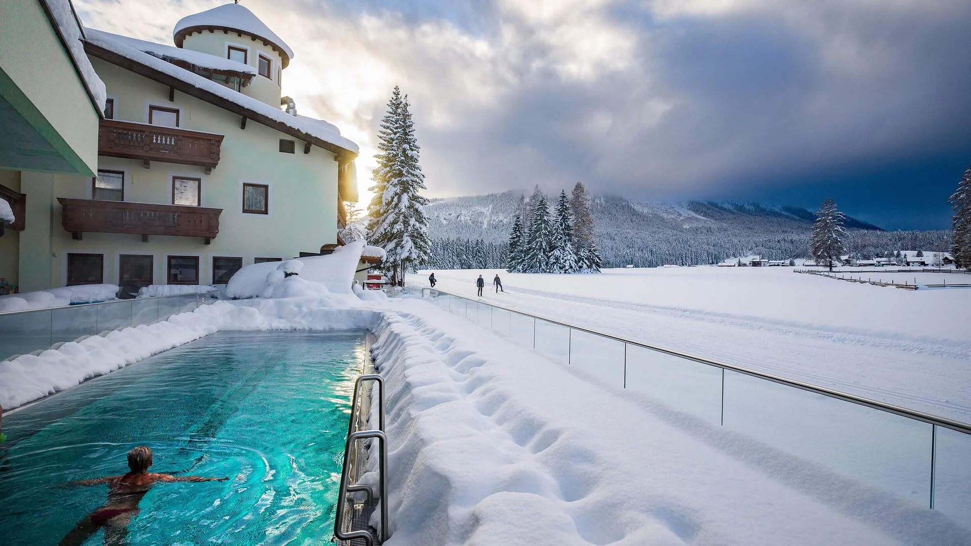 Person swimming in outdoor pool at hotel surrounded by snow-covered landscape