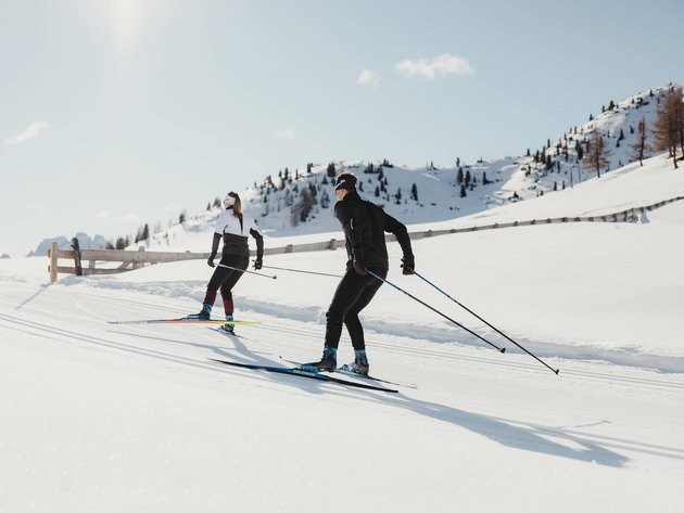 Zwei Skifahrer beim Langlaufen auf verschneiten Bergen bei Sonnenschein