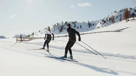 Two cross-country skiers on snowy mountains under bright sunlight