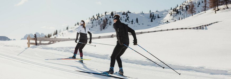 Zwei Skifahrer beim Langlaufen auf verschneiten Bergen bei Sonnenschein