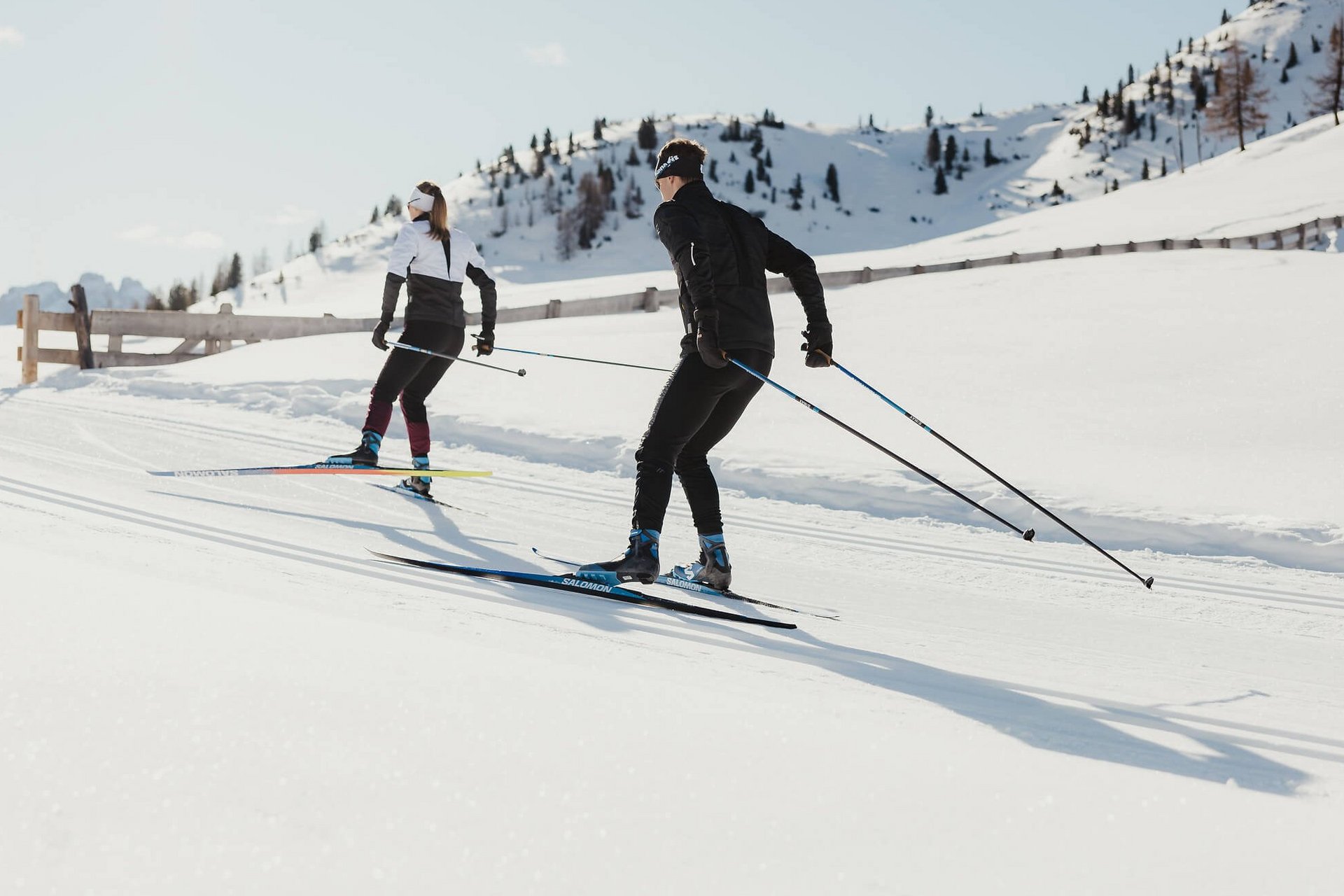Two cross-country skiers on snowy mountains under bright sunlight